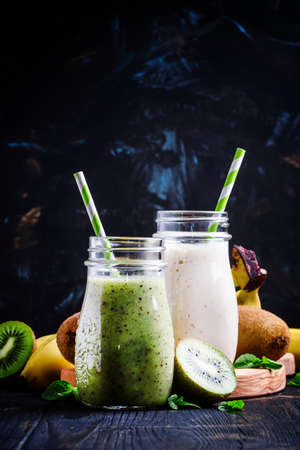 Kiwi and banana smoothies in bottles, black background, selective focusの写真素材