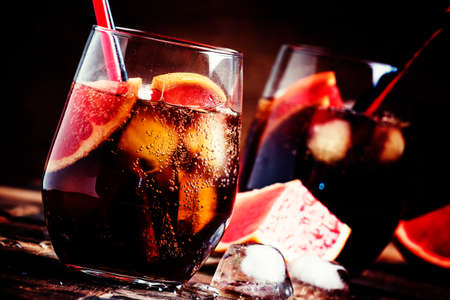Cocktail with cola, grapefruit juice, ice cubes and liqueur, dark vintage wooden background, selective focusの写真素材