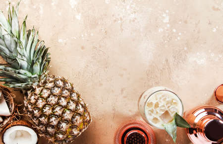 Pina Colada Cocktail on sand beige background with tropical fruits and bar tools, summer relaxation...
