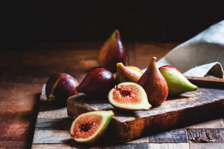 Cut purple figs on the board. Vintage wooden background, low key. Selective focus.の写真素材