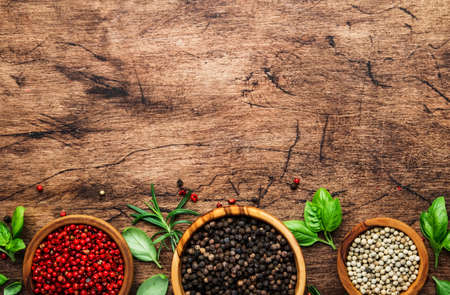 Black, white and pink rose peppers in bowls, assorted spices and spicy herbs on wooden rustic...