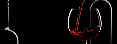 Pouring red wine into the glass against black background. Panoramic banner with copy spaceの写真素材