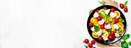 Salad of multi-colored tomatoes, mozzarella, and green basil, gray background, top view. Panoramic banner with copy spaceの写真素材