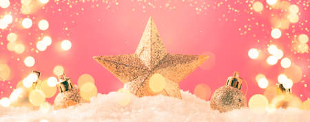Christmas pink background with golden star. New Year's decor. Christmas balls in snowdrifts and golden bokeh lights. Panoramic banner with copy spaceの写真素材