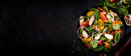 Spring salad with spinach, grilled chicken, cherry tomatoes, arugula, corn salad and red onion. Healthy food concept. Black stone table. Top view. Panoramic banner with place for textの写真素材