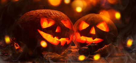 Halloween pumpkin head jack o lantern with burning fire and smoke background, wooden table with light bokeh garland. Beautiful Holiday Autumn Compositionの写真素材