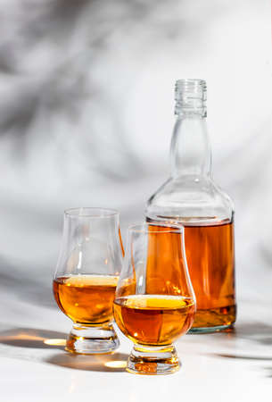 Scotch Whiskey without ice in glasses and bottle, white background with hard light, shadows and sun glare, copy spaceの写真素材