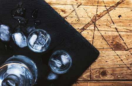 Vodka in shot glasses on wooden background, iced strong drink in misted glass. Top view