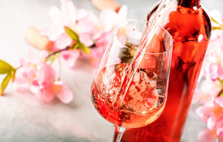 Rose wine pouring out of the bottle, gray background, pink flowers.の写真素材