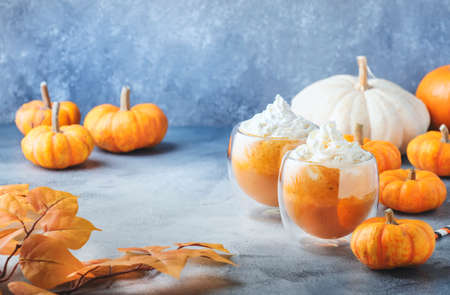 Pumpkin spiced latte or coffee in double glass cup on gray table. Autumn or winter hot drink in festive table settingの写真素材