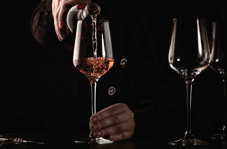Sommelier pouring rose wine into glass at wine tasting in winery, bar or restaurant. Dark backgroundの写真素材