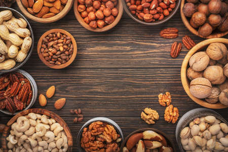 Assortment of nuts in bowls. Cashews, hazelnuts, walnuts, pistachios, pecans, pine nuts, peanuts, macadamia, almonds, brazil nuts. Food mix on wooden background, top view, copy spaceの写真素材