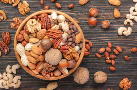 Assortment of nuts in bowls. Cashews, hazelnuts, walnuts, pistachios, pecans, pine nuts, peanuts, macadamia, almonds, brazil nuts. Food mix on wooden background, top view, copy spaceの素材 [FY310165079254]