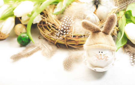 Spring Easter holiday white background with tulips, bunny, quail eggs, butterflies and feathers in a nest. Banner with copy space. Top viewの写真素材