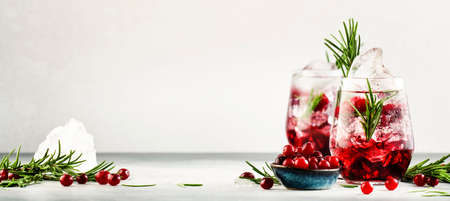 Cranberry cocktail or mocktail with ice, rosemary and red berries in tumbler glass, gray backgroundの写真素材
