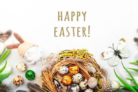 Spring Easter holiday white background with tulips, quail eggs, butterflies, bunny and feathers in a nest. Banner with copy space. Top viewの写真素材