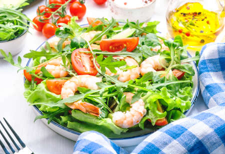 Fresh shrimp salad with tomatoes, lettuce, arugula, avocado, cucumber and lemon dressing on white background. Healthy eating, clean food concept. Top viewの写真素材