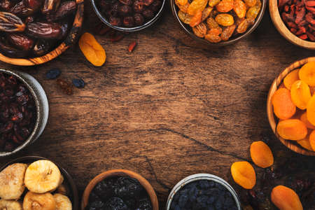 Healthy food snack: dried fruits, natural sun dried organic mix of dried apricots, figs, raisins, dates, cranberries, cherries, goji berries, prunes in bowls on wooden background, top viewの写真素材