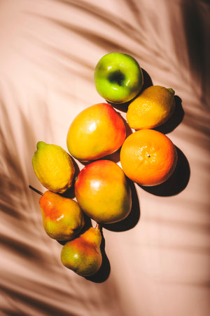 Summer fruits top view. Contemporary still life, pale pink background, hard light and palm leaves shadow patternの写真素材