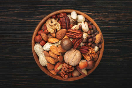 Assortment of nuts in bowls. Cashews, hazelnuts, walnuts, pistachios, pecans, pine nuts, peanuts, macadamia, almonds, brazil nuts. Food mix on wooden background, top view, copy spaceの写真素材
