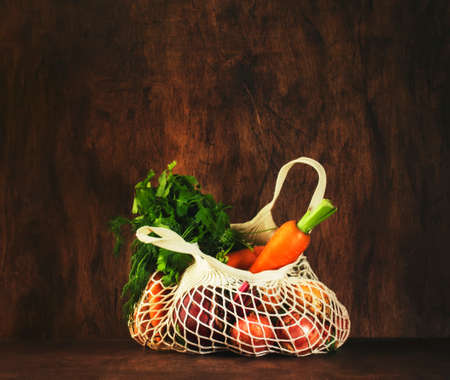 Mesh bag with vegetables and herbs on wood background. Modern reusable shopping, eco friendly lifestyle, zero waste conceptの写真素材