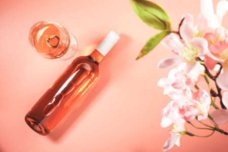 Rose wine glass with bottle on blush background and pink flowers. Rosado, rosato pink wine tasting