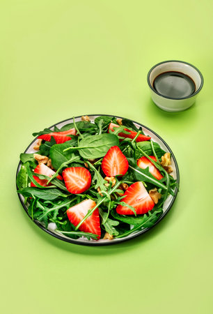 Strawberry Vegan Salad with spinach, arugula, walnuts, balsamic vinegar and olive oil dressing on lime green background. Healthy food. Top viewの写真素材