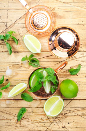 Moscow mule alcoholic cocktail in copper mug with lime, ginger beer, vodka and mint. Wooden bar counter, bartender work tools, top viewの写真素材