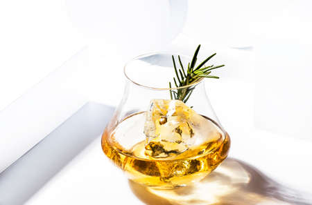 Whiskey or bourbon glass with rosemary, shard ice on white background with geometric cubes and circles. Contemporary still lifeの写真素材