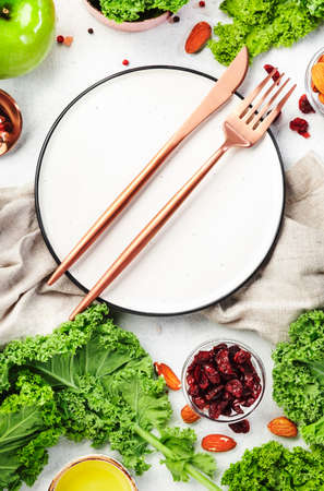 Kale salad preparing. Empty plate. Dried cranberry, green apples, spices, dressing and walnuts. Healthy vegan food, top view, gray kitchen tableの写真素材