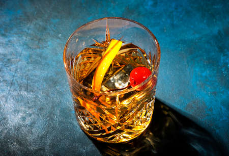 Old fashioned alcoholic cocktail with bourbon whiskey, marascino cherry and orange peel garnish, blue table, copy space, top view, hard lightの写真素材