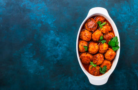 Meatballs with spicy tomato sauce in white baking dish on blue kitchen table. Top Viewの写真素材