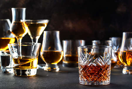 Hard strong alcoholic drinks, spirits and distillates in glasses in assortment: vodka, cognac, scotch, whiskey etc. Brown bar counter backgroundの写真素材