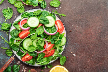 Spring vegan salad with spinach, cherry tomatoes and red onion. Healthy food concept. Brown stone table.Top view. Copy spaceの写真素材