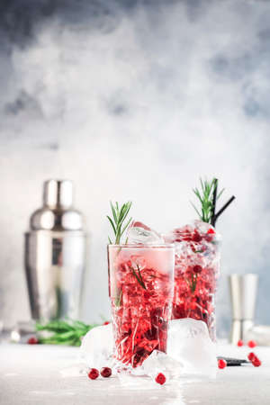 Cranberry cocktail with vodka, ice, juice, rosemary and red berries in highball glass. Refreshing long drink. Gray table background with negative spaceの写真素材