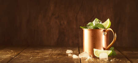 Moscow mule cocktails in copper mug with lime, ice, ginger beer, vodka and mint. Wooden background, bar tools, negative spaceの写真素材