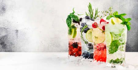 Cocktails drinks. Classic alcoholic long drink or mocktail highballs with berries, lime, herbs and ice on gray backgroundの写真素材