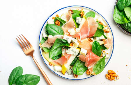 Pear salad with prosciutto, blue cheese, spinach, walnuts on white background, top view, copy spaceの写真素材