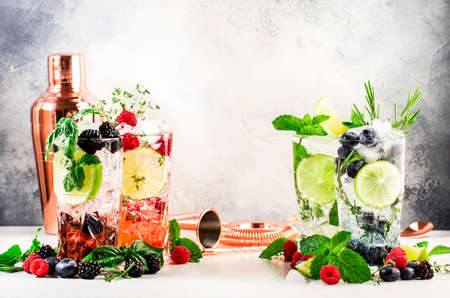 Cocktails drinks. Classic alcoholic long drink or mocktail highballs with berries, lime, herbs and ice on gray backgroundの写真素材