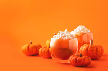 Orange pumpkin latte with whipped cream in glass cup. Autumn or winter hot drink in festive table...