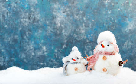 Christmas and new year snow concept with two cute snowmen in hats and scarves in snowdrift on blue backgroundの写真素材
