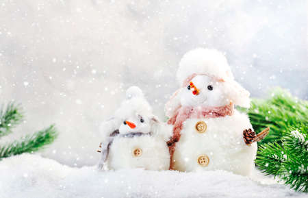 Christmas and new year snow concept with two cute snowmen in hats and scarves in snowdrift with fir branches and xmas decor on gray backgroundの写真素材
