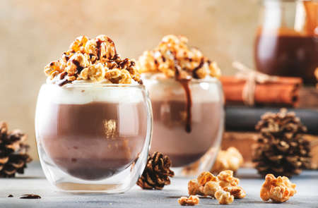 Cold winter chocolate dessert with whipped cream, popcorn and caramel topping in glasses on beige background, place for textの写真素材