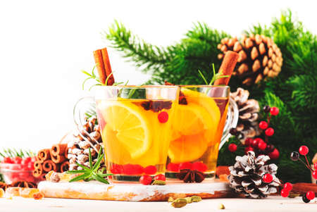 Winter hot tea with lemon, cranberries, herbs and spices in Christmas or New Year table setting, white background, copy spaceの写真素材