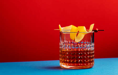 Sazerac, classic alcoholic cocktail with cognac, bourbon, absinthe, bitters, sugar and lemon zest. Dazzling red blue background with hard light and harsh shadowsの写真素材