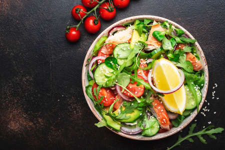 Fresh Salad with chicken, tomatoes, arugula, onion, avocado, sesame seeds and lemon oil dressing. Healthy food. Top view. Brown tableの写真素材