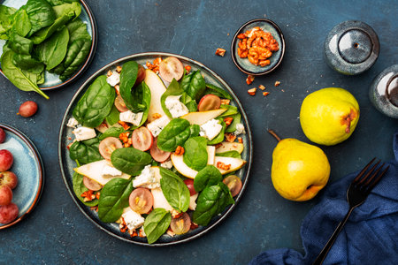 Fresh salad with pear, grapes, blue cheese, spinach, walnuts on blue table background, top view, copy spaceの写真素材