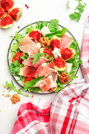 Fresh fig salad with prosciutto, gorgonzola, walnuts, arugula on white kitchen table background, top view, copy spaceの写真素材