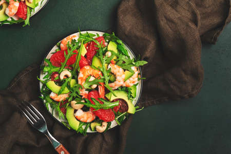 Delicious salad with shrimps, avocado, grapefruit, arugula and cashews. Low key dark green table background, top view, negative spaceの写真素材