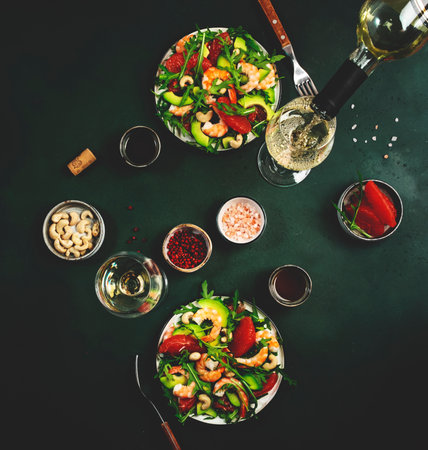 Delicious salad with shrimps, avocado, grapefruit, arugula and cashews. Low key dark green table background, top view. Served table for two persons with glasses of white wineの素材 [FY310182626257]